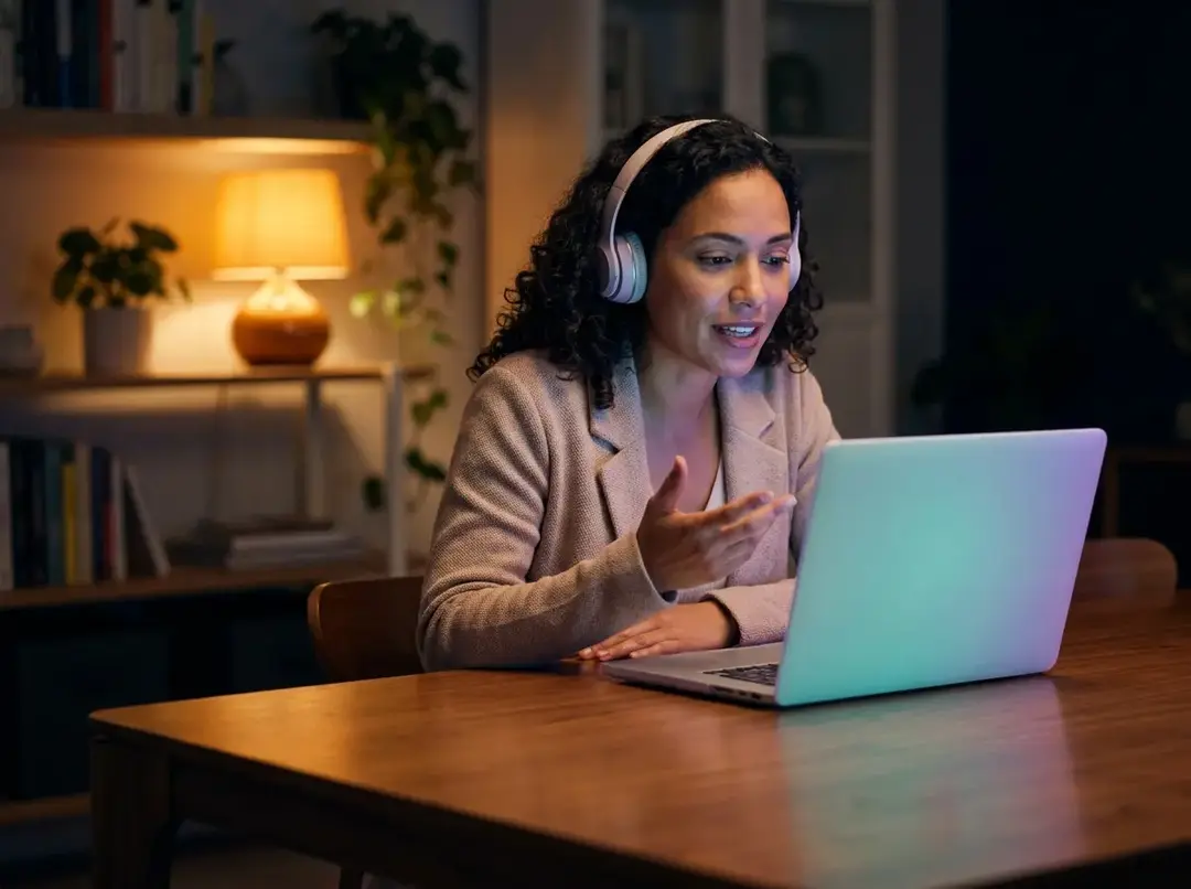 Mujer estudiando inglés en vivo desde su casa por la noche, con audífonos y laptop